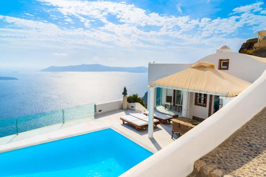 SANTORINI ISLAND, GREECE - MAY 24, 2015: A view of caldera with luxury house and pool in foreground, typical white architecture of Imerovigli village on Santorini island, Greece. Source: Shutterstock